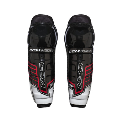 Jambières de hockey CCM Next 26 pour petits enfants, vue de face de la paire avec le logo CCM NEXT sur la coque