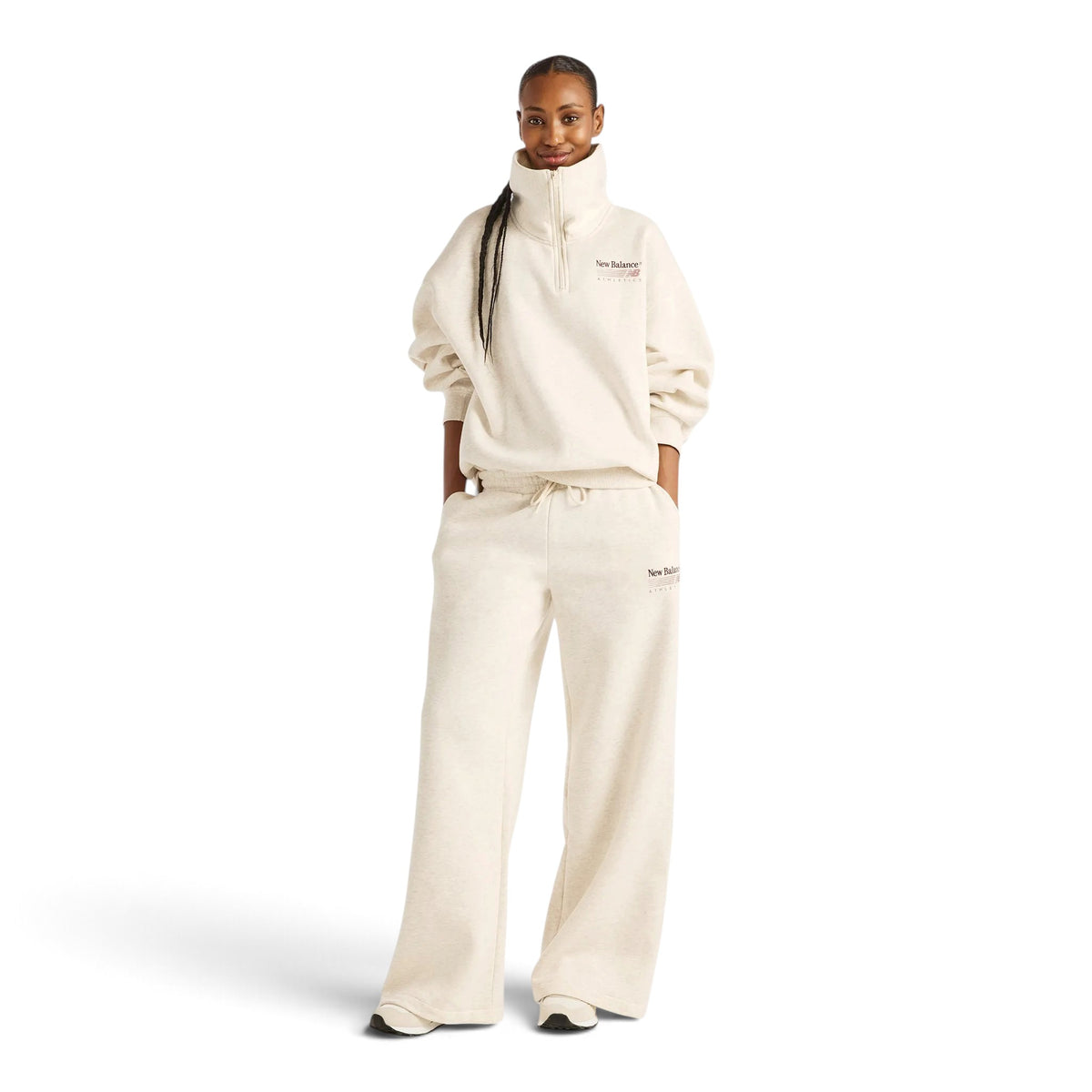 Femme en pied portant le pantalon New Balance Trackside beige avec un haut à col montant assorti