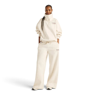 Femme en pied portant le pantalon New Balance Trackside beige avec un haut à col montant assorti